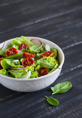 salad with fresh vegetables, garden herbs and sun-dried tomatoes in a white bowl on a dark wooden background