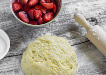 dough, strawberry, sugar - ingredients for making strawberry pie on a light wooden background
