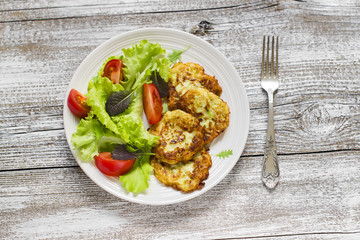 zucchini pancakes and fresh vegetable salad on white plate on a light wooden background