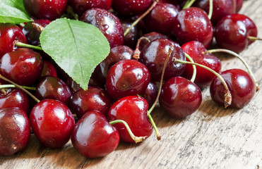 Many black fresh cherries with leaves on the old wooden table, s