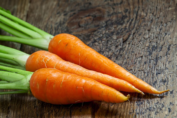 Fresh carrots with tops on old wooden table, selective focus