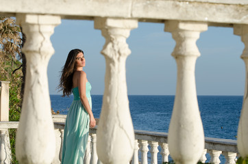 Beautiful lady standing on veranda of a beachfront home, ocean as background