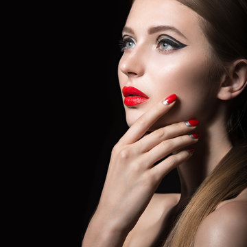 Beautiful girl with unusual black arrows on eyes and red lips and nails. Beauty face. Picture taken in the studio on a black background.