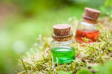 Two bottles of essential oil or magic potion on moss in forest
