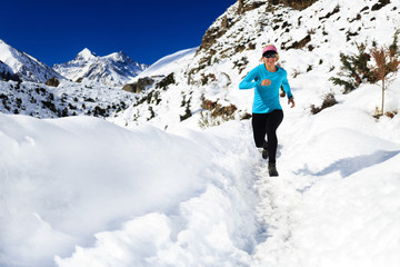 Fototapeta na wymiar Woman trail running on snow in winter mountains