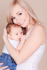 Happy mother holding baby boy. Smiling woman with her newborn child over beige. Motherhood