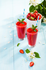 Strawberry smoothie and flower petals on blue background