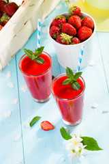 Strawberry smoothie and flower petals on blue background