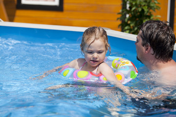Child girl in bikini bathing in the pool with his father