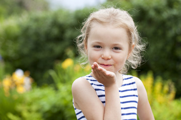 Blonde little Girl Blowing a Kiss, on summer park background