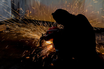 Silhouettes of Worker and sparks of bonfire while grinding iron