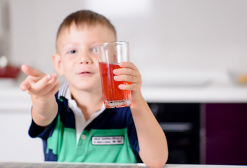 Young Boy Holding Glass of Red Juice Toward Camera