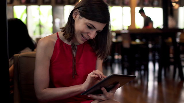 Happy woman using tablet computer and drinking coffee in cafe
