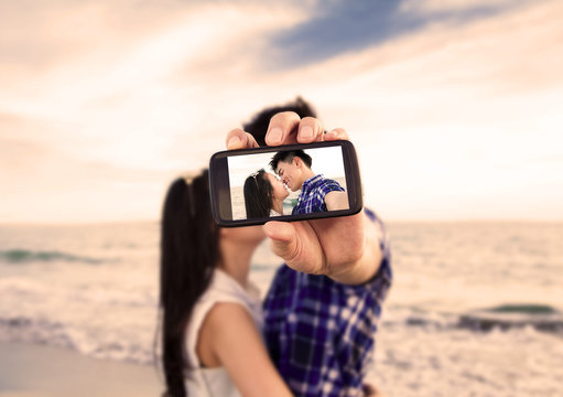 Couple taking self portrait photos with smart phone on the beach