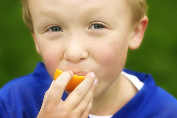 Close up of a young boy eating an orange outside