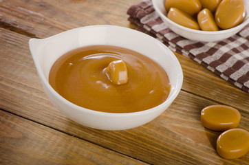 Caramel candies and sauce on   rustic wooden background.