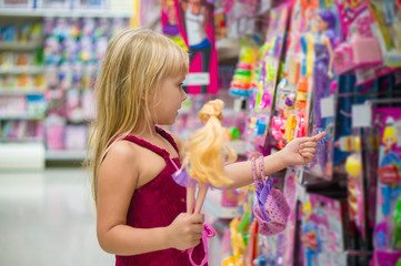 Adorable girl select dolls in toy section of supermarket