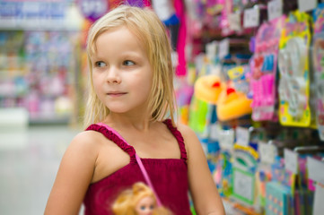Adorable girl select dolls in toy section of supermarket