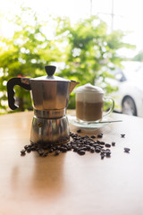 a moka pot and a cup of coffee with roasted coffee beans