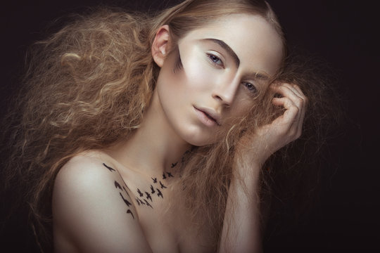 Beautiful girl with a pattern on the body in the form of birds, creative makeup and hairstyle lush. Beauty face. Picture taken in the studio on a gray background.