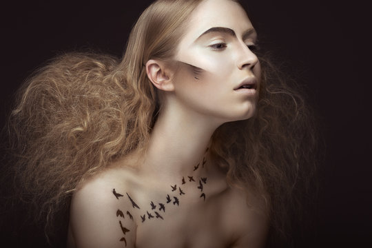 Beautiful girl with a pattern on the body in the form of birds, creative makeup and hairstyle lush. Beauty face. Picture taken in the studio on a gray background.