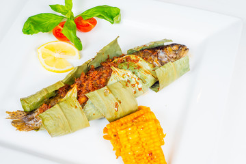 Fish baked in leaves and served on a white plate