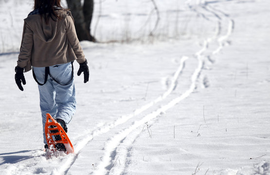 young woman walking with two orange snowshoes in mountains in wi