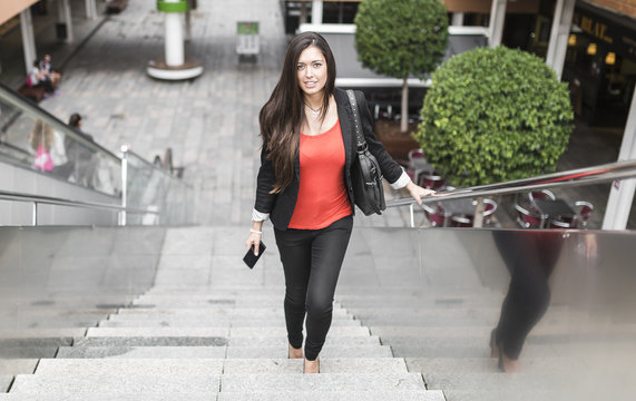 Portrait of a beautiful young businesswoman walking up stairs wi