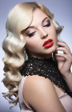 Beautiful blonde in a Hollywood manner with curls, red lips and lace dress. Beauty face. Picture taken in the studio on a white background.