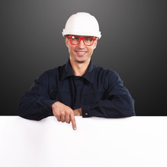 Smiling workman in dark blue coveralls pointing at the blank copy space