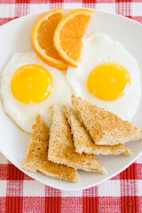 Eggs for Breakfast – A plate of two sunny-side up eggs, toast triangles, and orange slices.