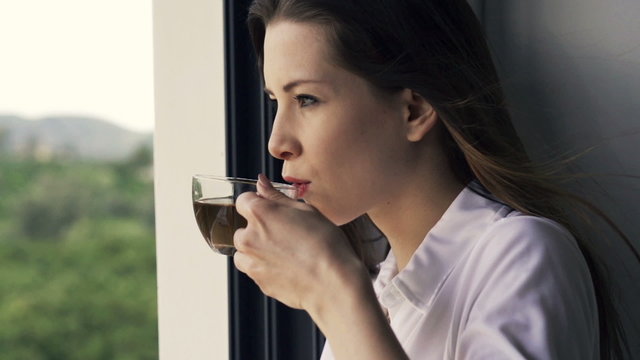 Young woman drinking tea standing by window at home, slow motion shot at 240fps
