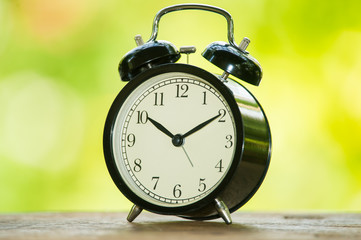 Alarm clock on table with blur green leaf background.