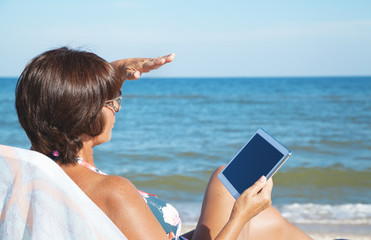 Elderly woman with tablet on beach
