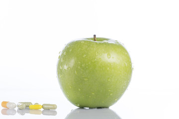Green apple and various colored pills on white background