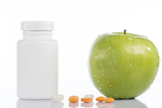 Natural green apple and various colored pills on white