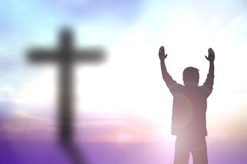Silhouette of man with raised hands over blur cross concept for