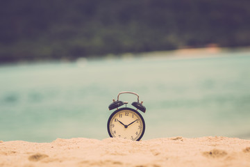 Concept time to travel. Alarm clock on beautiful beach. Retro filter.