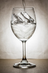 Pouring drinking water in wine glass with ice in warm tone