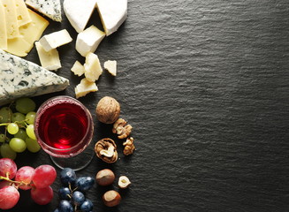 Different types of cheeses with wine glass and fruits.