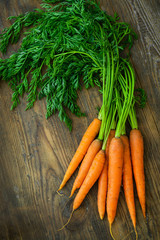 Bunch of fresh carrots with green leaves over wooden background