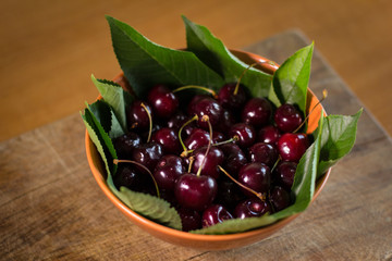 Ripe cherries in bowl on wooden plank