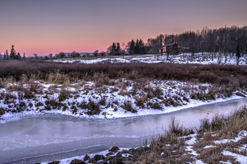 Frozen stream in middle of winter at sunrise with snow in field