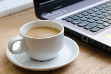 Cup of coffee and laptop on wooden table.