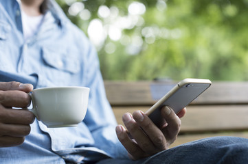 Men are using a smart phone while drinking a coffee in a park bench