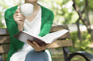 Women have a reading with a cup of coffee in the park - obrazy, fototapety, plakaty
