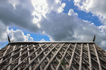 Fototapeta na wymiar Thatch roof and rainy clouds and sun behind clouds