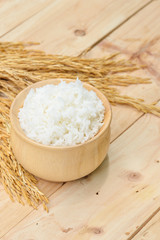 bowl full of rice and ear of rice on wooden background