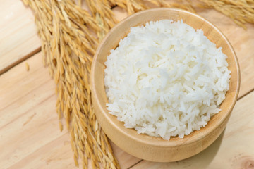 bowl full of rice and ear of rice on wooden background