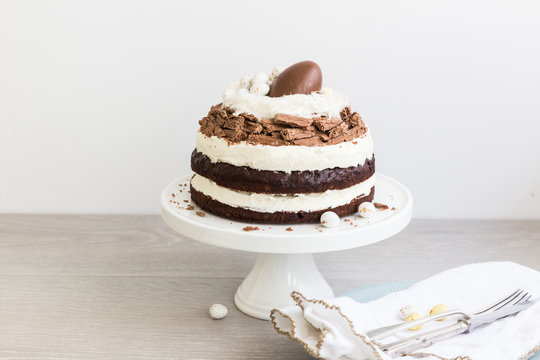 Chocolate layer cake decorated with chocolate Easter eggs, chocolate flakes and whipped cream on a cake stand